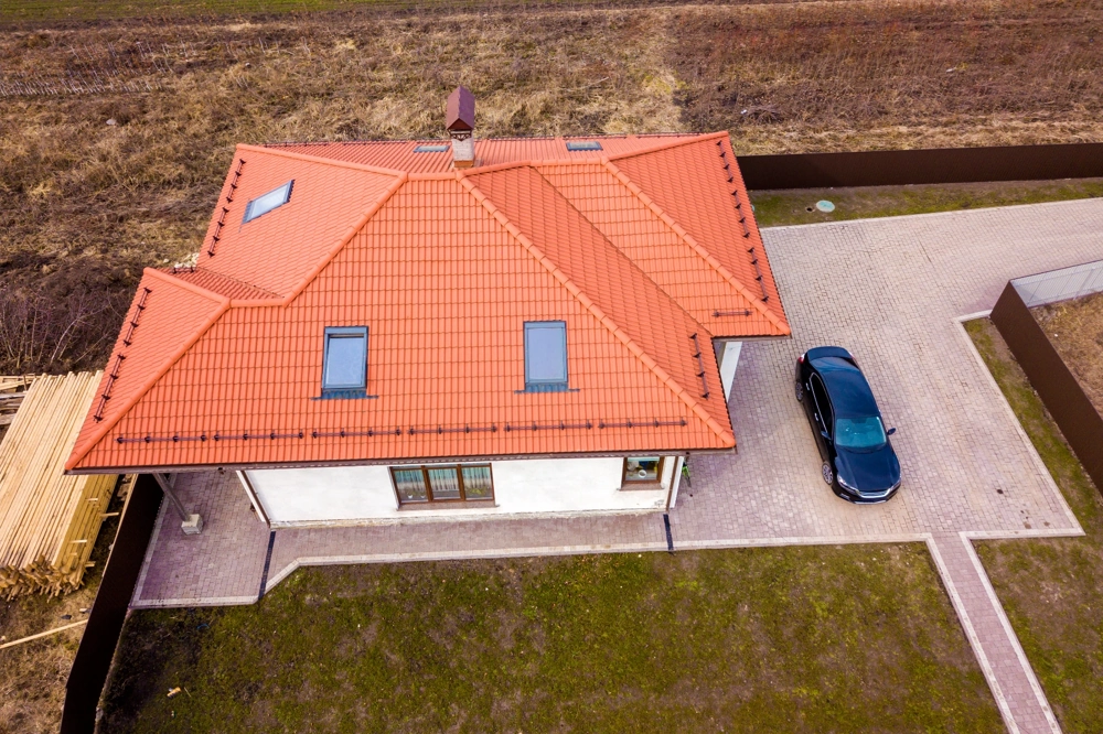 Układanie kostki brukowej wokół domu na podjeździe z ogrodem i trawnikiem widziane z góry