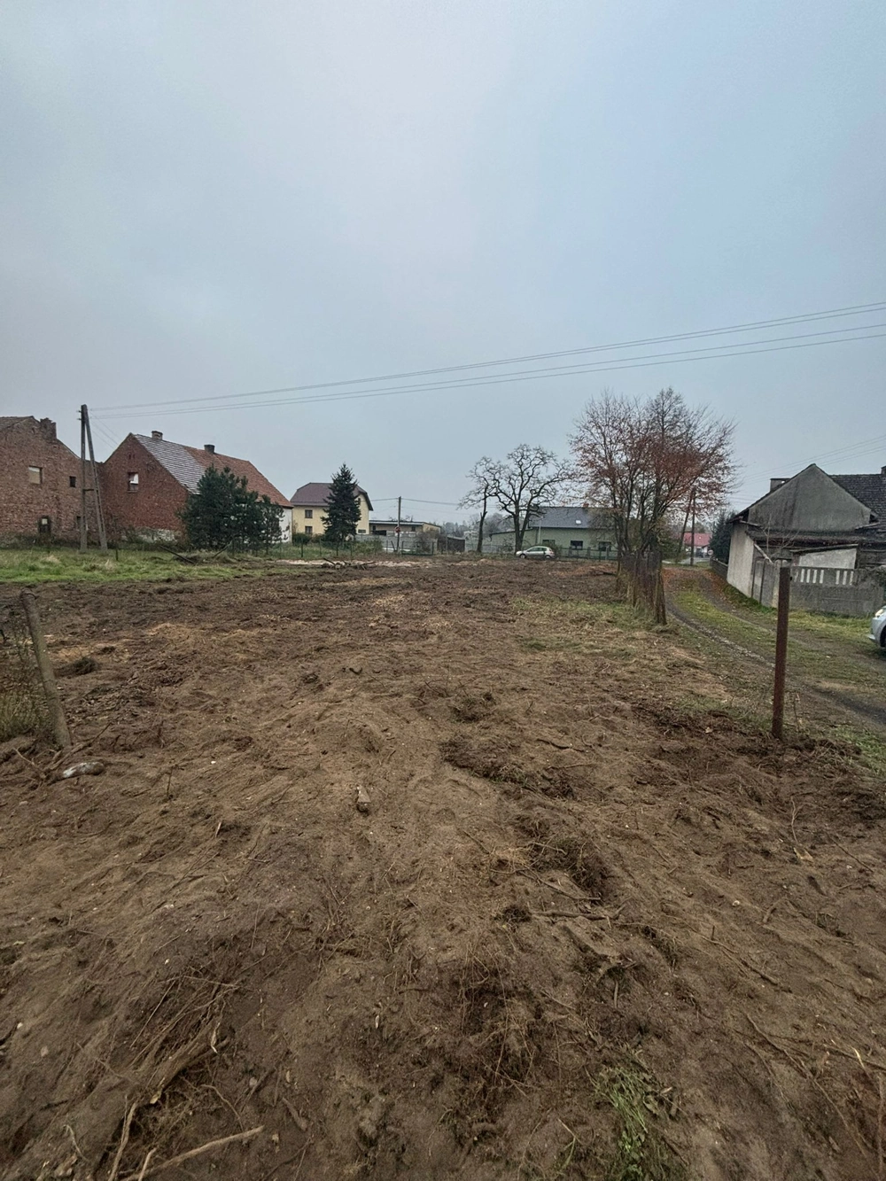 Wyrównany teren działki z usuniętą roślinnością przy domach – usługa Karczowanie działki