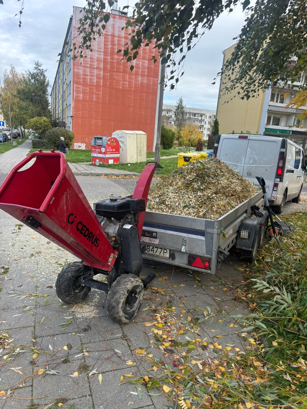 Rębarka rozdrabnia gałęzie i liście, trociny trafiają do przyczepy obok auta – Usługi rębakiem
