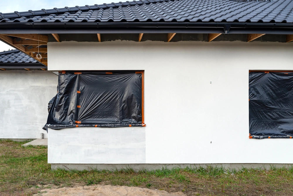 Okna domu zabezpieczone folią podczas malowania elewacji