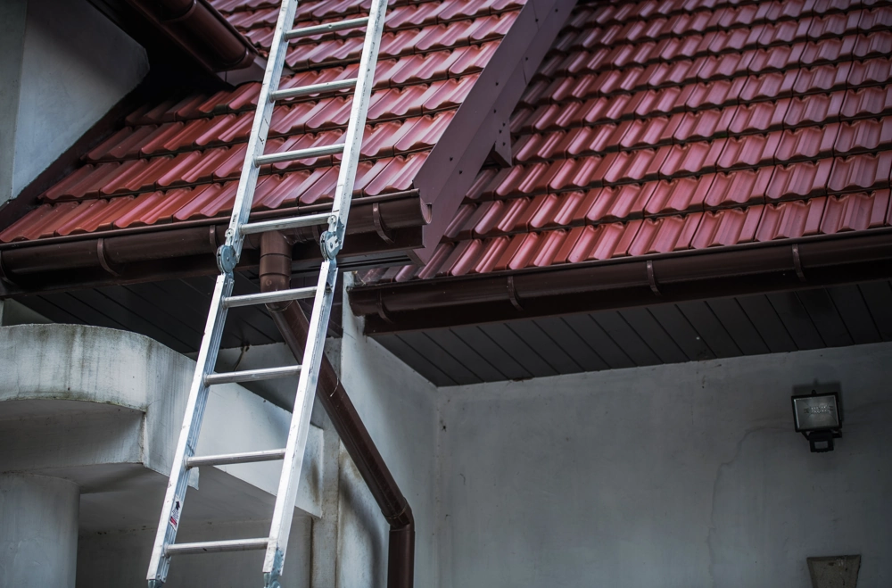 Drabina oparta o czerwony dach z dachówkami ceramicznymi